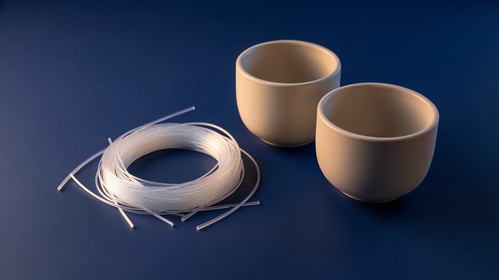 A coil of thin translucent fibers rests beside two plain open tan ceramic bowls on a matte blue surface.