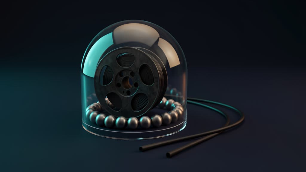 A black metal reel and a ring of silver beads sit under a clear glass dome, with two plain black cable ends resting outside.